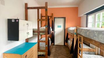 A dormitory room with bunk beds, a dresser, a wardrobe, and a window with a view.