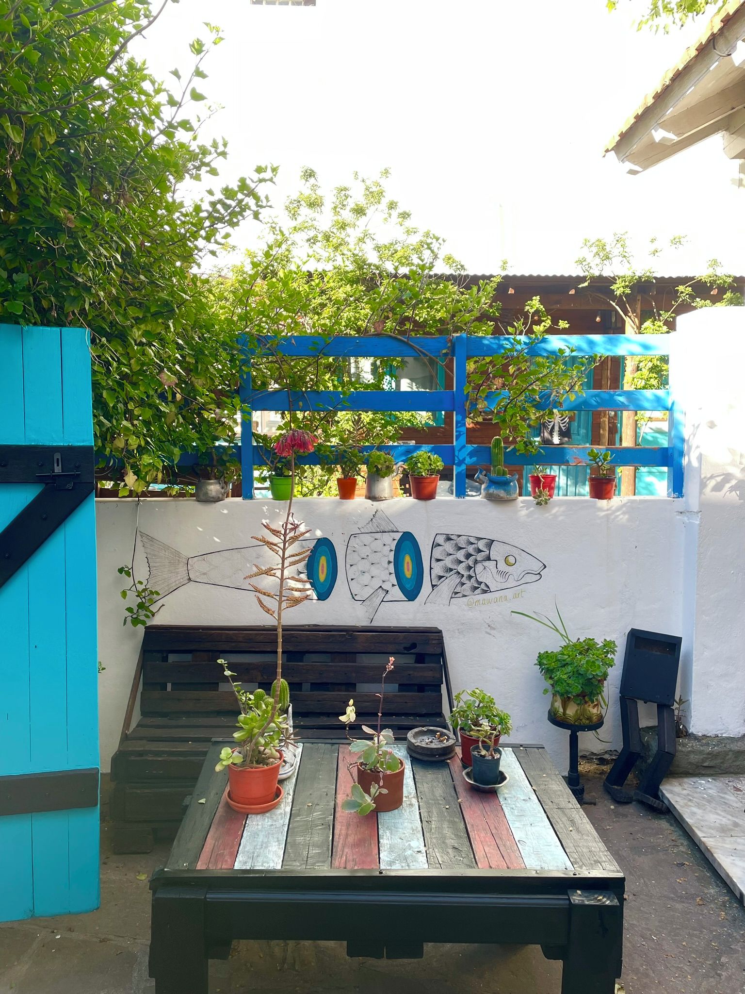 A patio area with a wooden table, potted plants, and a wall mural.