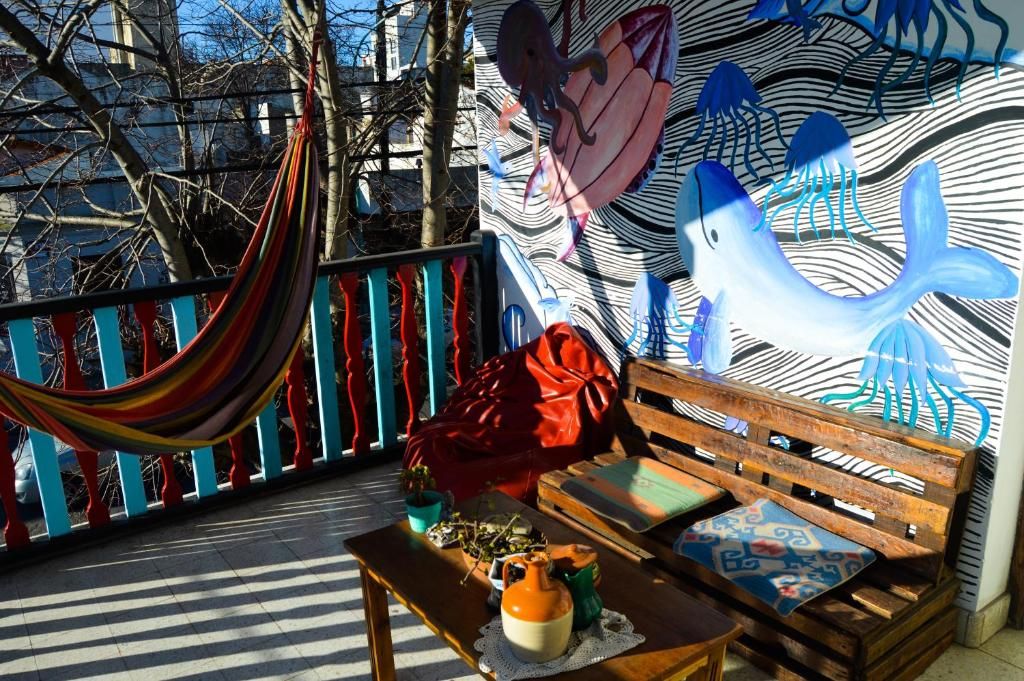 Una hamaca, un banco y una mesa con varios objetos en un balcón con un mural de fondo.