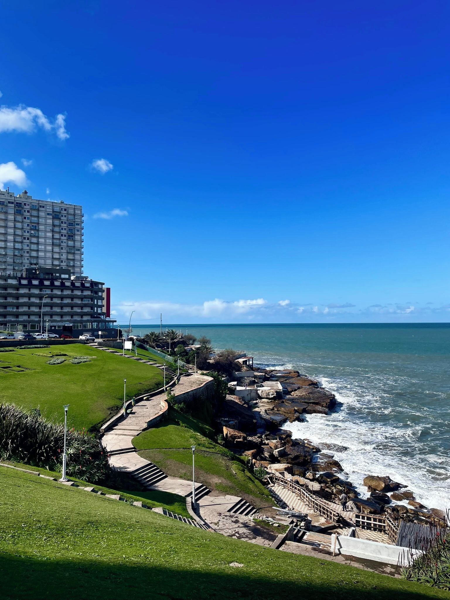 A coastal hotel with a view of the sea, a promenade, and a large building in the background.