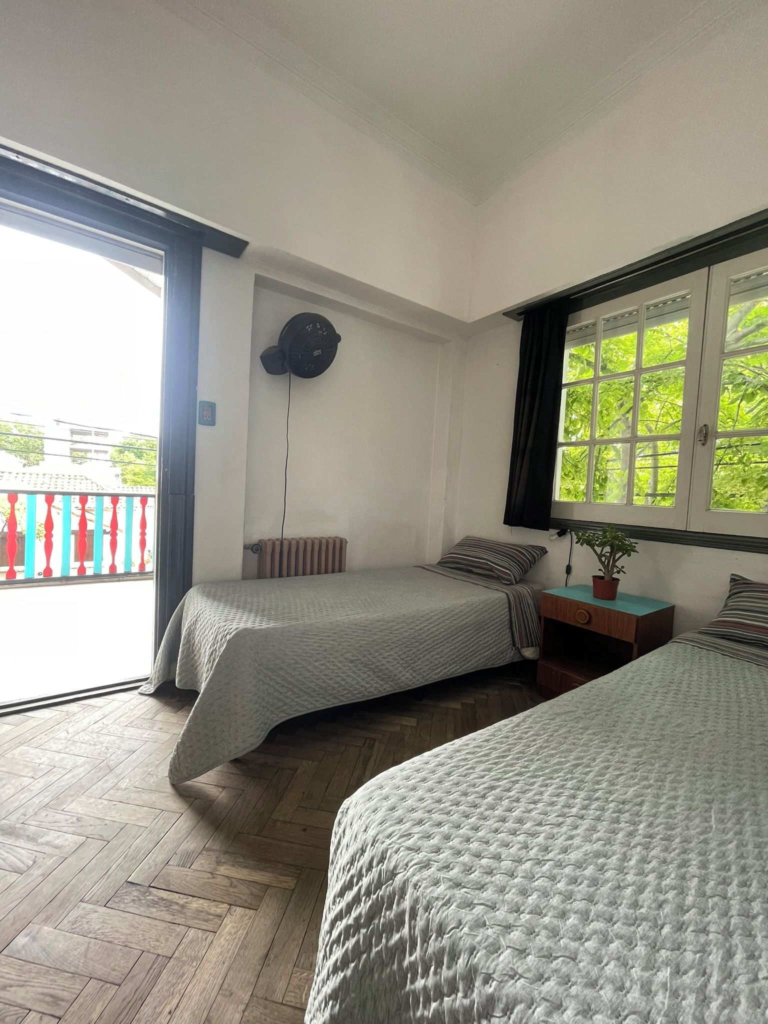 Habitación con dos camas, un radiador, un ventilador de techo y una ventana con vistas a follaje.