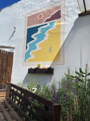 A wall with a colorful mural, a wooden bench, and various plants.