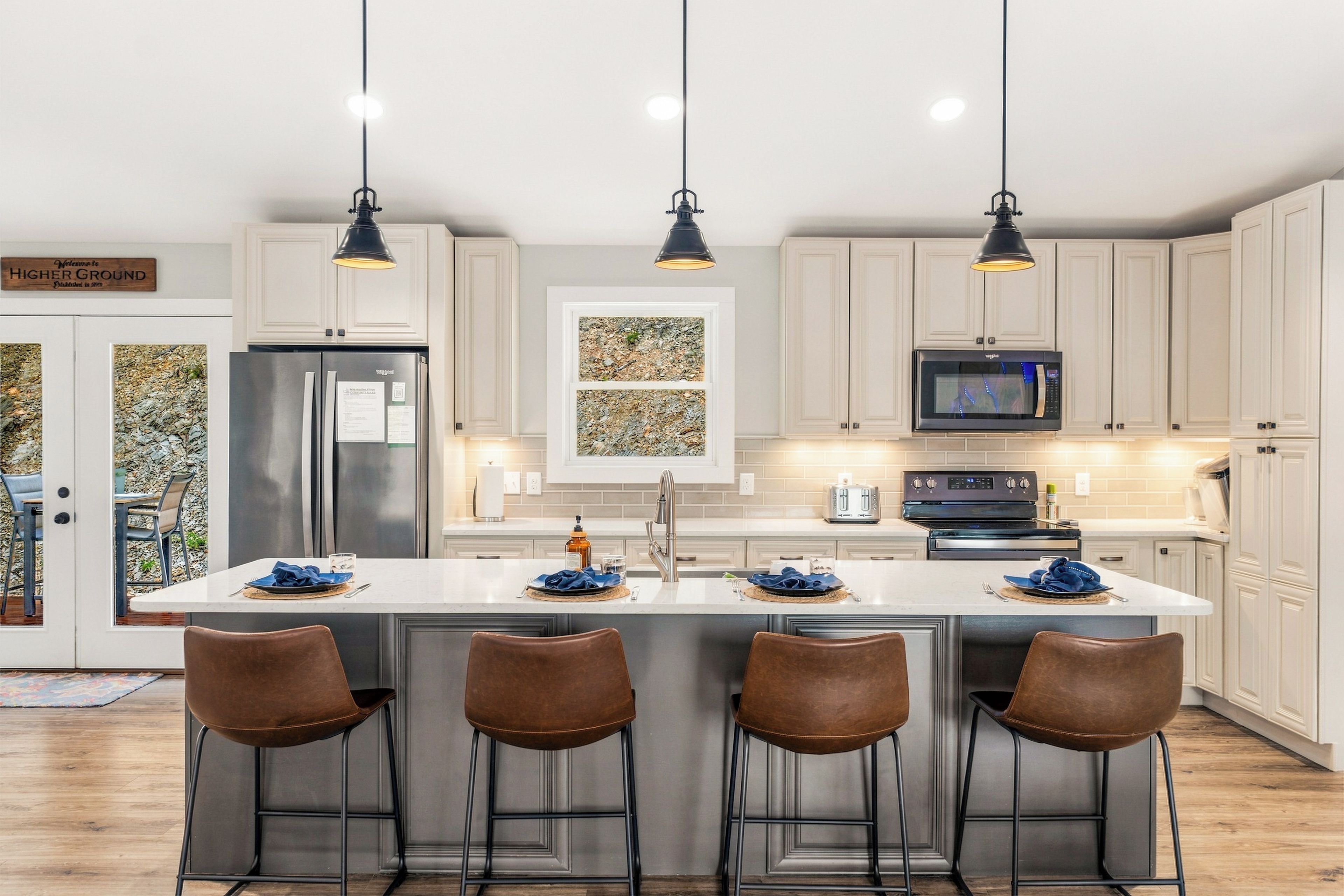 Een moderne keuken met witte kastjes, een roestvrijstalen koelkast, een magnetron en een centraal eiland met barstoelen.