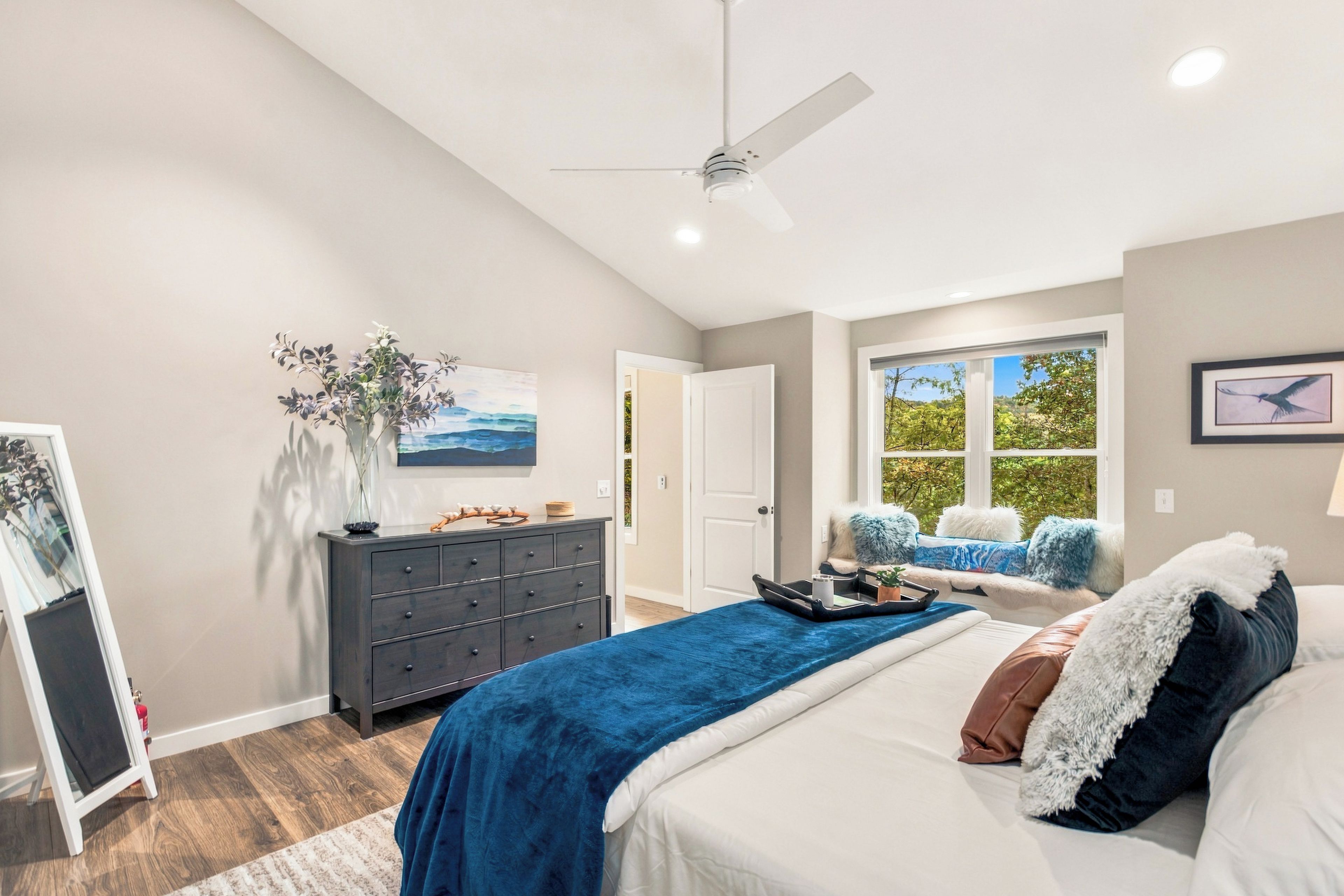 Een slaapkamer met een bed, een dressoir en een raam met uitzicht op bomen.