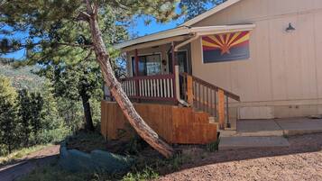 A building with a wooden staircase leading to a porch, a flag on the side, and a tree in front.