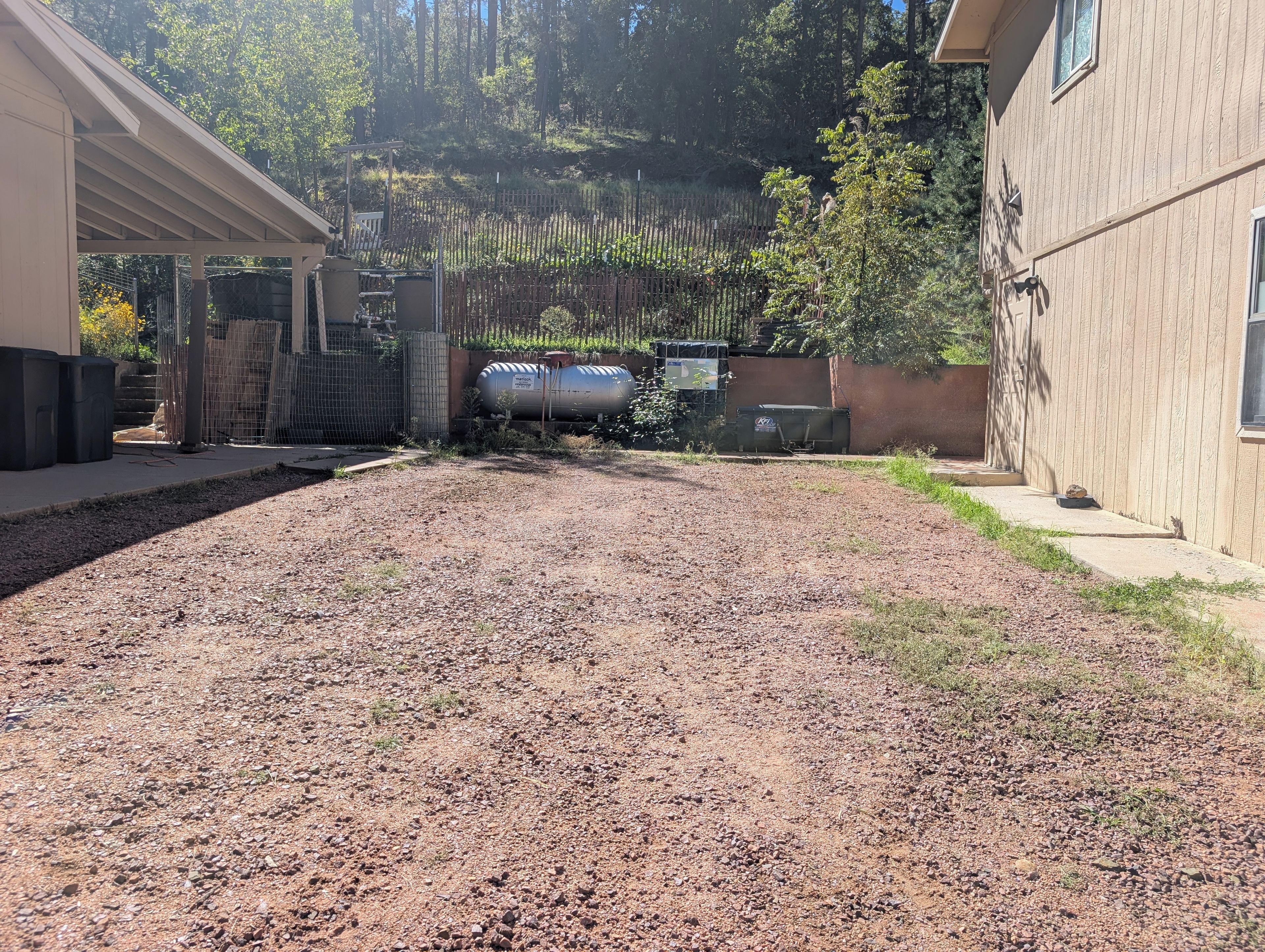 A gravel driveway leading to a fenced area with a building on the right and a covered structure on the left.