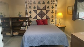 A bedroom with a bed, a bookshelf, a wall tapestry, a lamp, and a window with blinds.