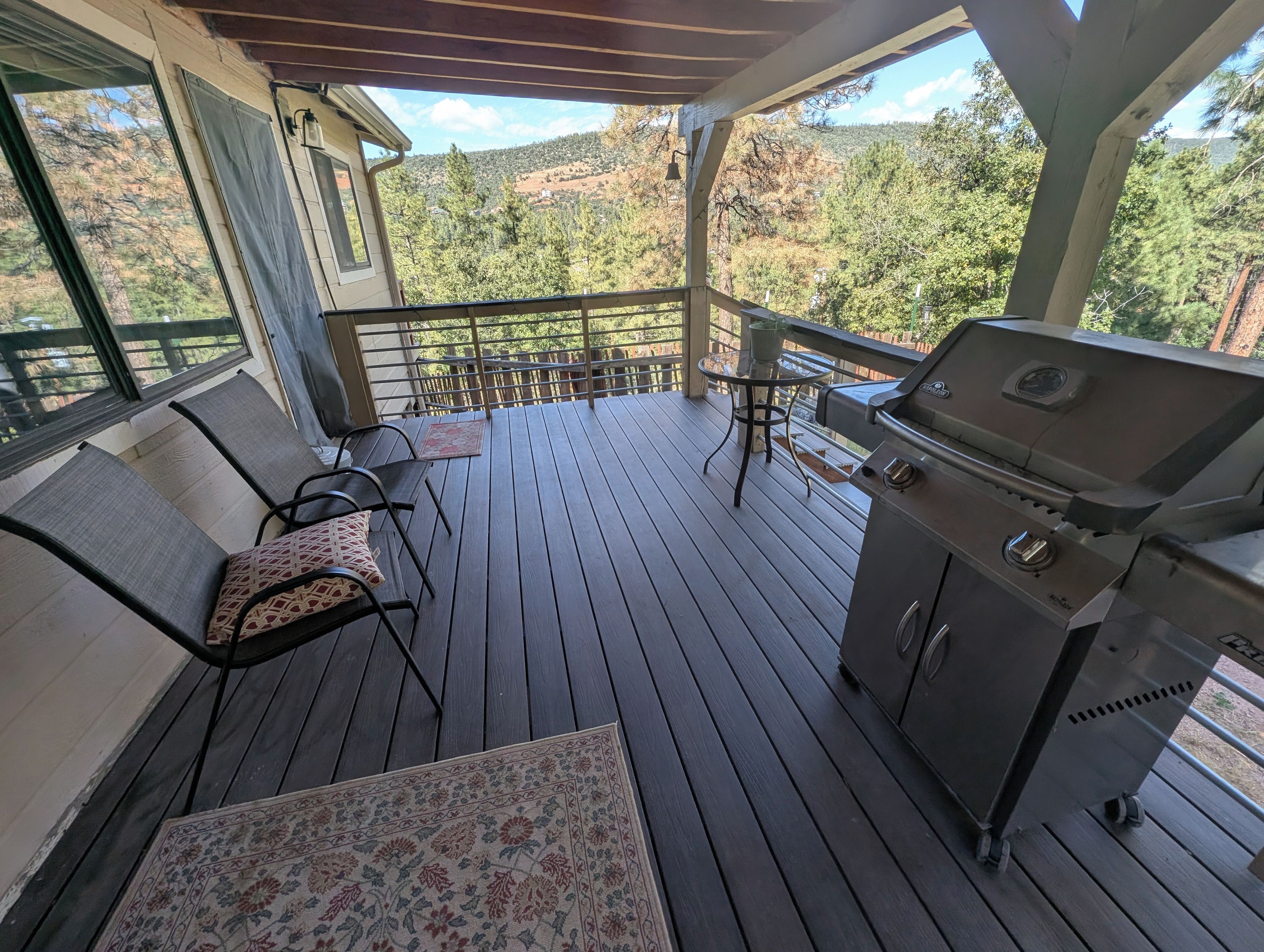 Eine überdachte Terrasse mit Grill, Stühlen und einem Tisch.