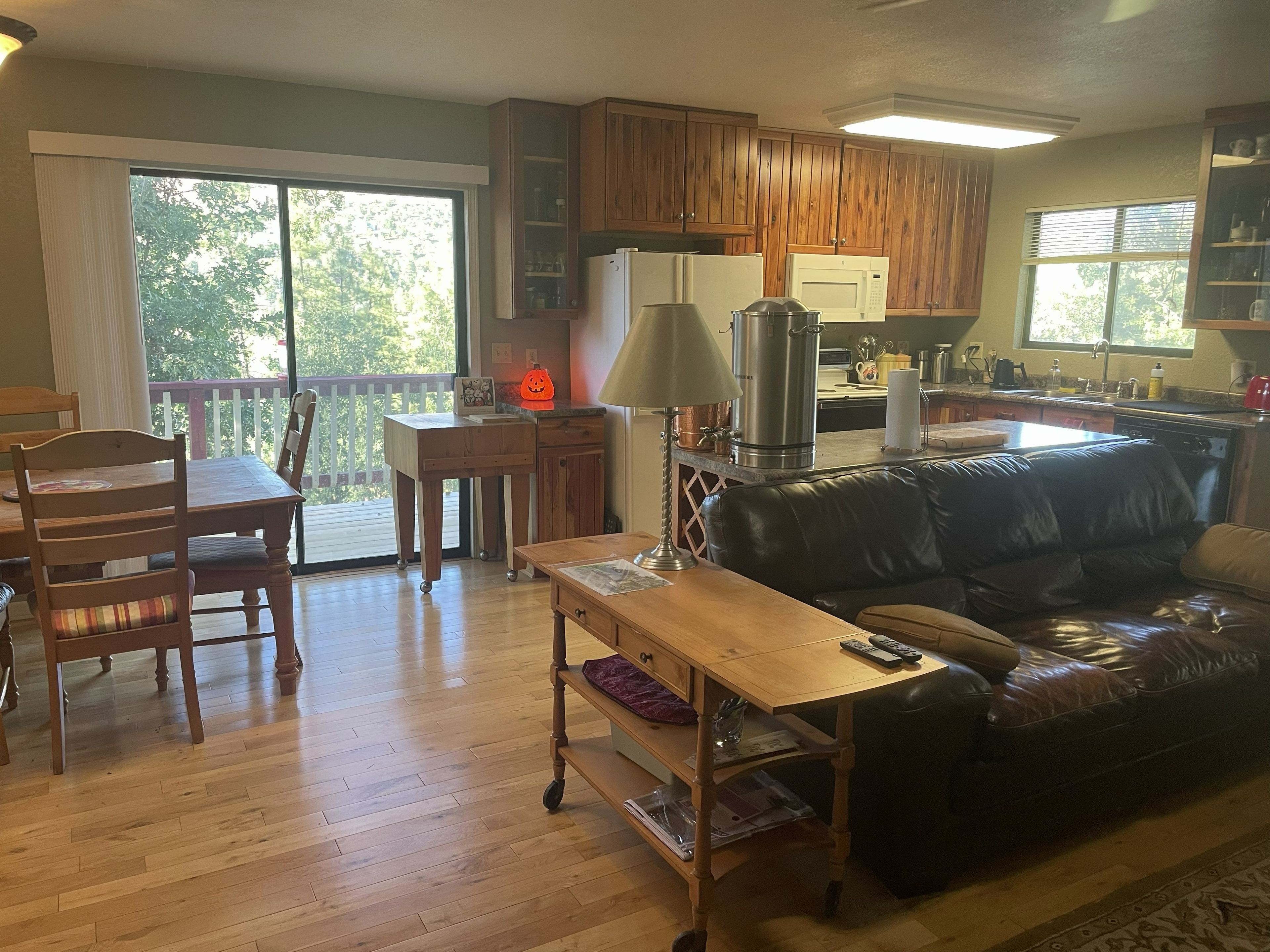 A living room with a wooden floor, a black leather sofa, a wooden coffee table, and a dining area with a wooden table and chairs.