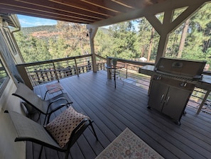 Una terrassa exterior coberta amb una barbacoa, zona de seients i vista a un paisatge boscós.
