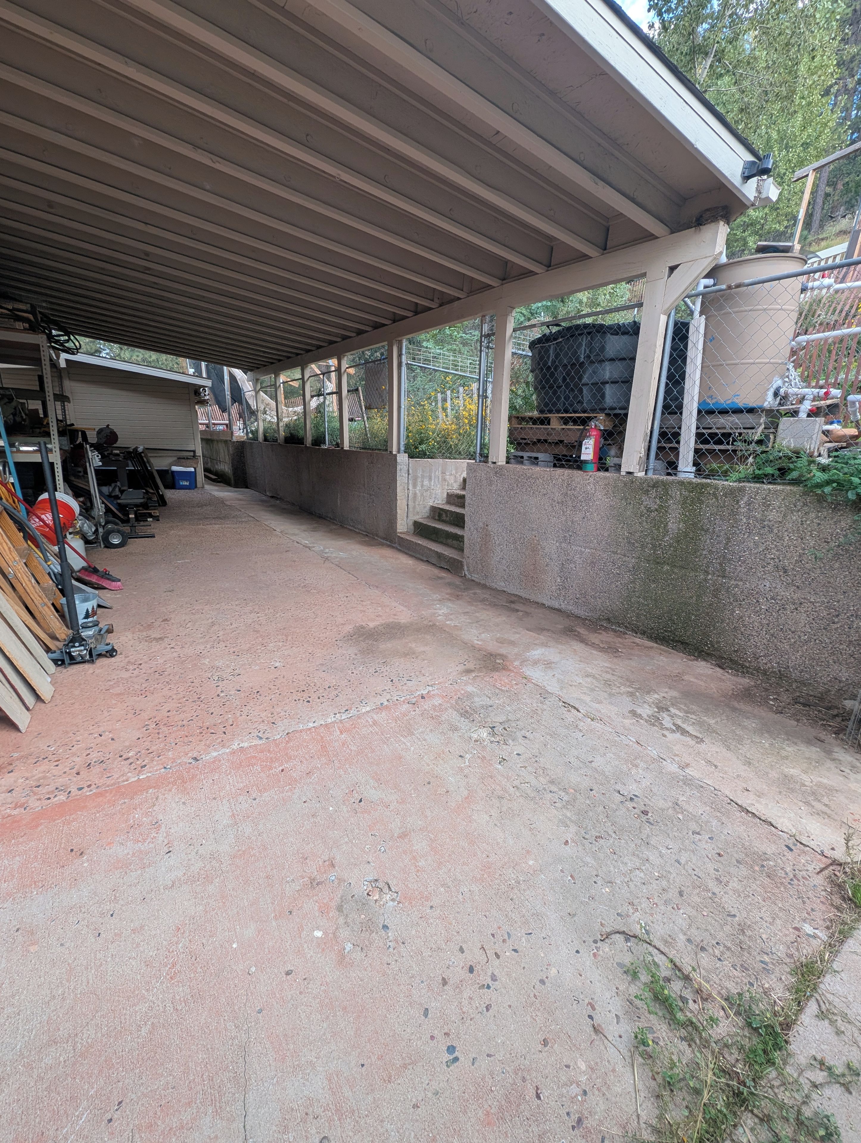 Un espace extérieur abrité, doté d’un sol en béton, d’une clôture en métal et d’un escalier menant à un niveau supérieur.