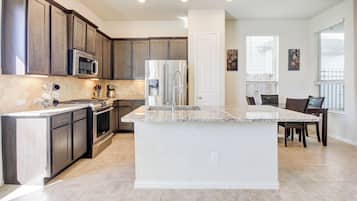 A modern kitchen with dark wood cabinets, stainless steel appliances, a granite countertop island, and a dining area with a table and chairs.