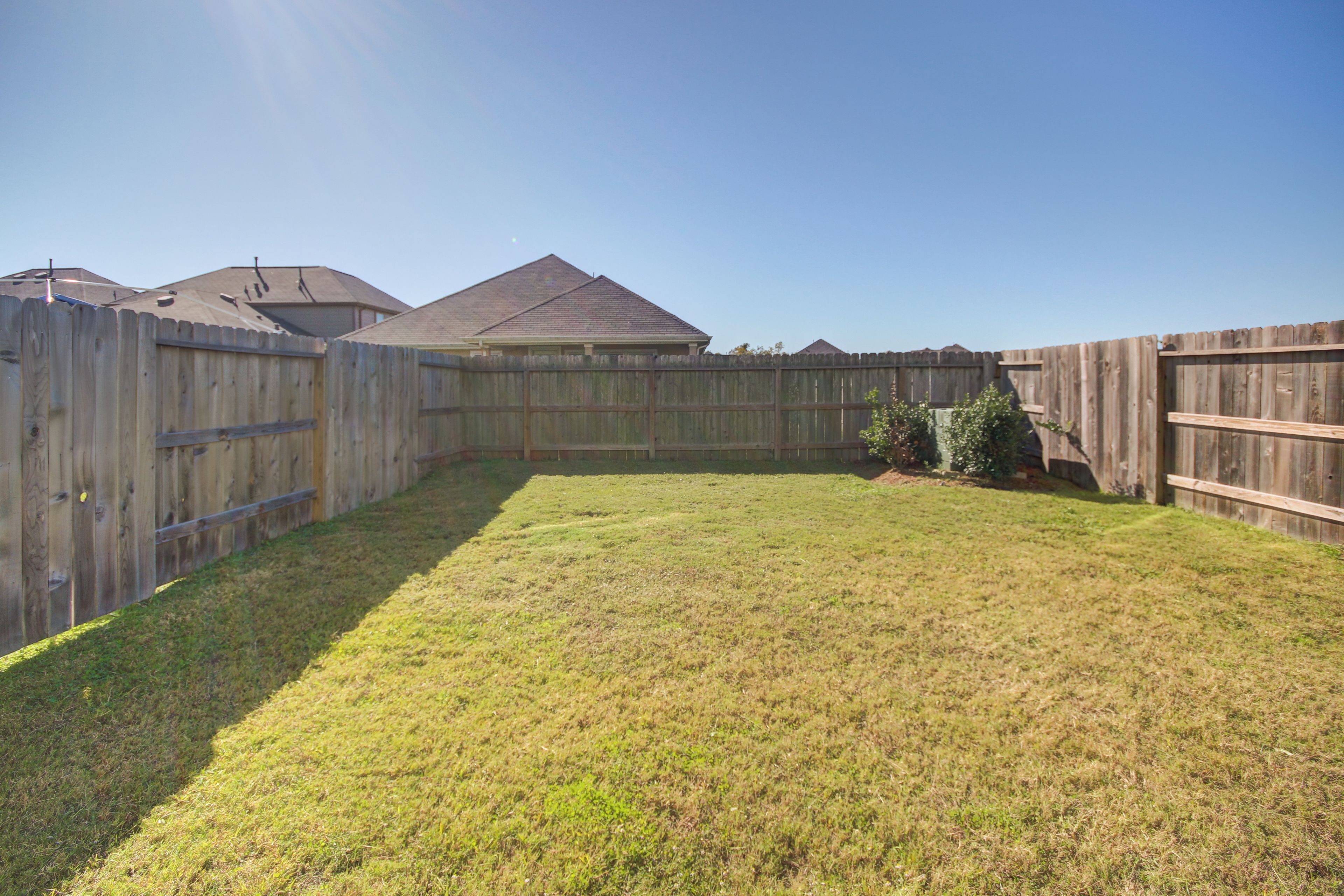 A backyard with a wooden fence, a grassy lawn, and a house with a gabled roof.