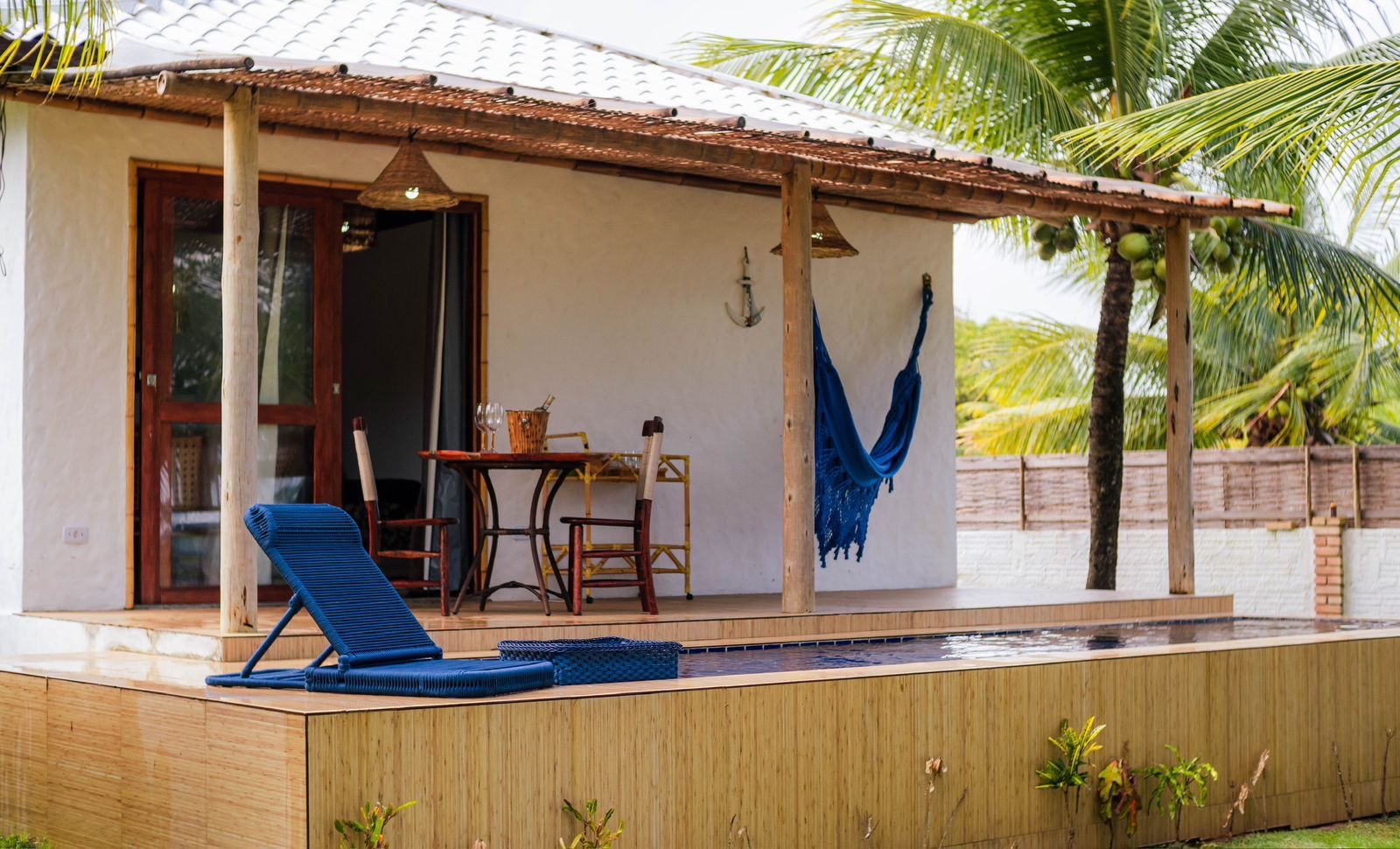 A covered outdoor area with a pool, lounge chairs, and a dining table.
