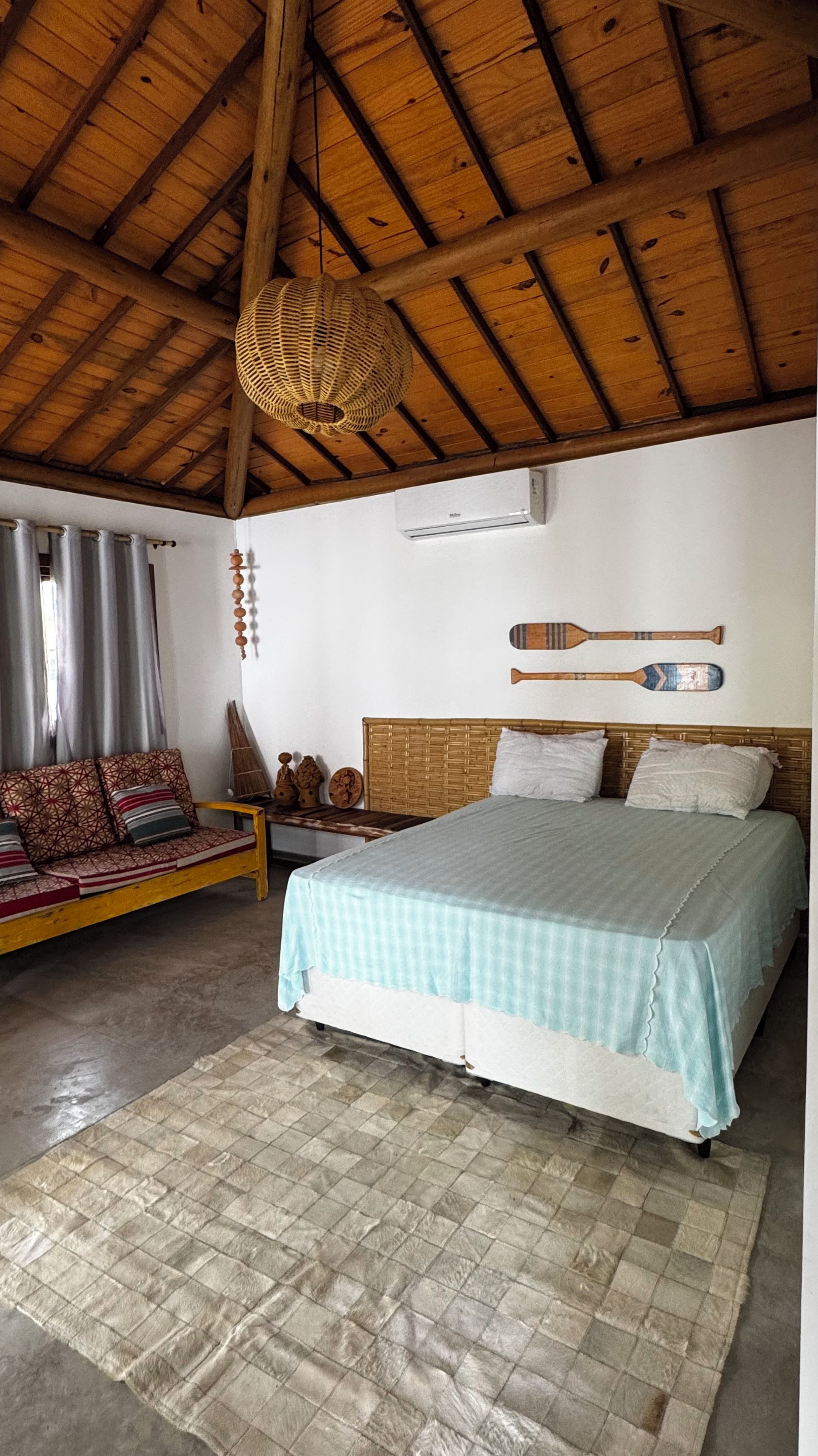 A room with a bed, a sofa, a woven ceiling light, and a wall-mounted air conditioner.