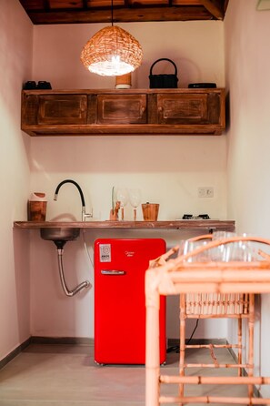 A kitchen with a red refrigerator, wooden cabinets, a hanging light fixture, and a bamboo chair. - New Listing (Japaratinga)