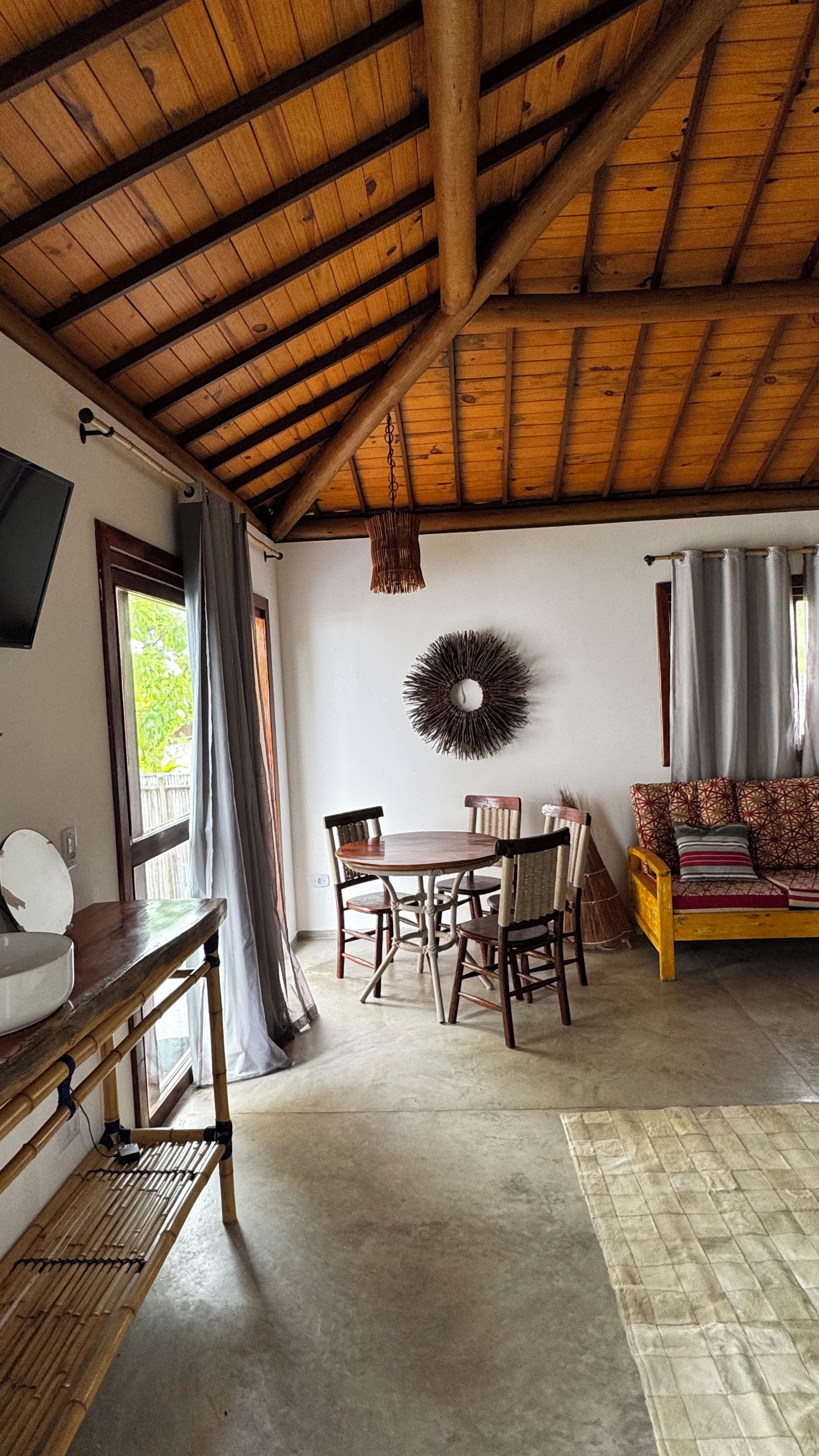 A rustic interior with a wooden ceiling, a round dining table with chairs, a sofa, and a wall-mounted decorative item.