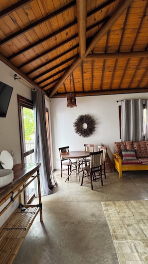 A rustic interior with a wooden ceiling, a round dining table with chairs, a sofa, and a wall-mounted decorative item. - New Listing (Japaratinga)