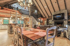 A spacious cabin interior with a dining area, a fireplace, and a television mounted on a stone wall. - Mountaintown Creek Lodge | Ellijay, GA (Gilmer County)