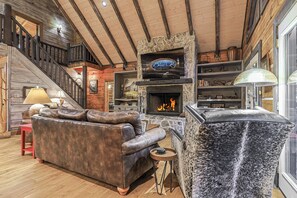 A cabin interior with a stone fireplace, leather sofa, and a television mounted on the wall. - Mountaintown Creek Lodge | Ellijay, GA (Gilmer County)