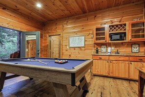 Un interior de madera con mesa de billar, armarios y una puerta que da al exterior.