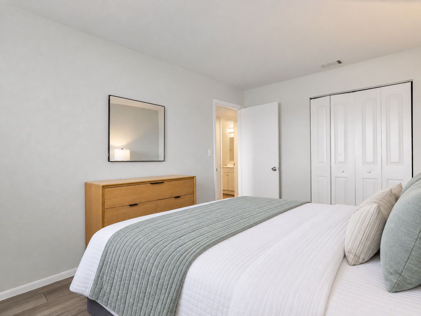 Ein Schlafzimmer mit einem Bett, einem Schminktisch, einem Spiegel und einer Tür zu einem Badezimmer.