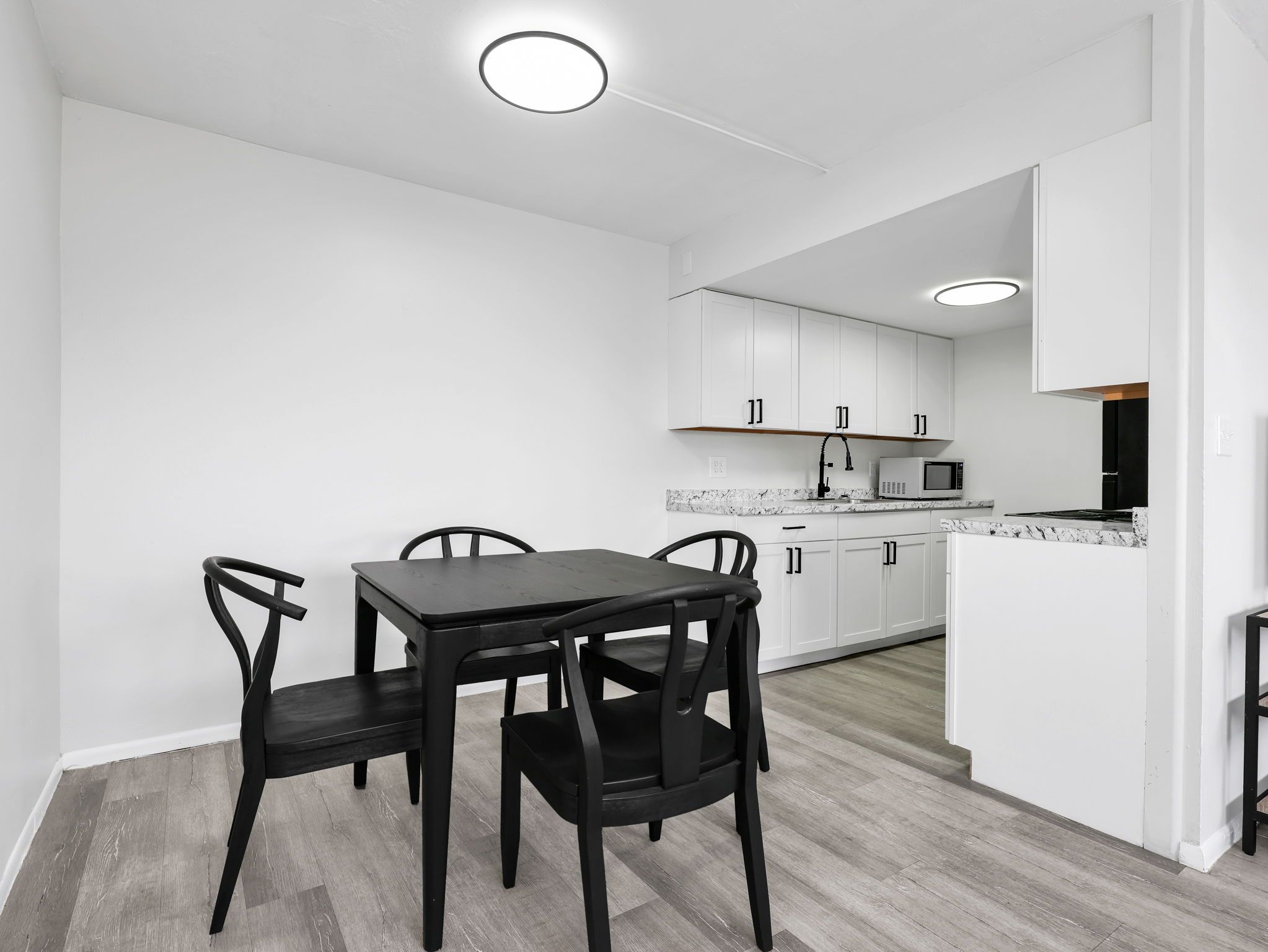 Una cocina moderna con armarios blancos, un comedor con mesa negra y sillas.