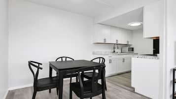 Una cocina moderna con armarios blancos, un comedor con mesa negra y sillas.