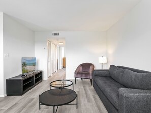 A modern living room with a sofa, armchair, coffee table, and TV stand. - Experience Elevated Living in Fort Myers 2 BR (Fort Myers)