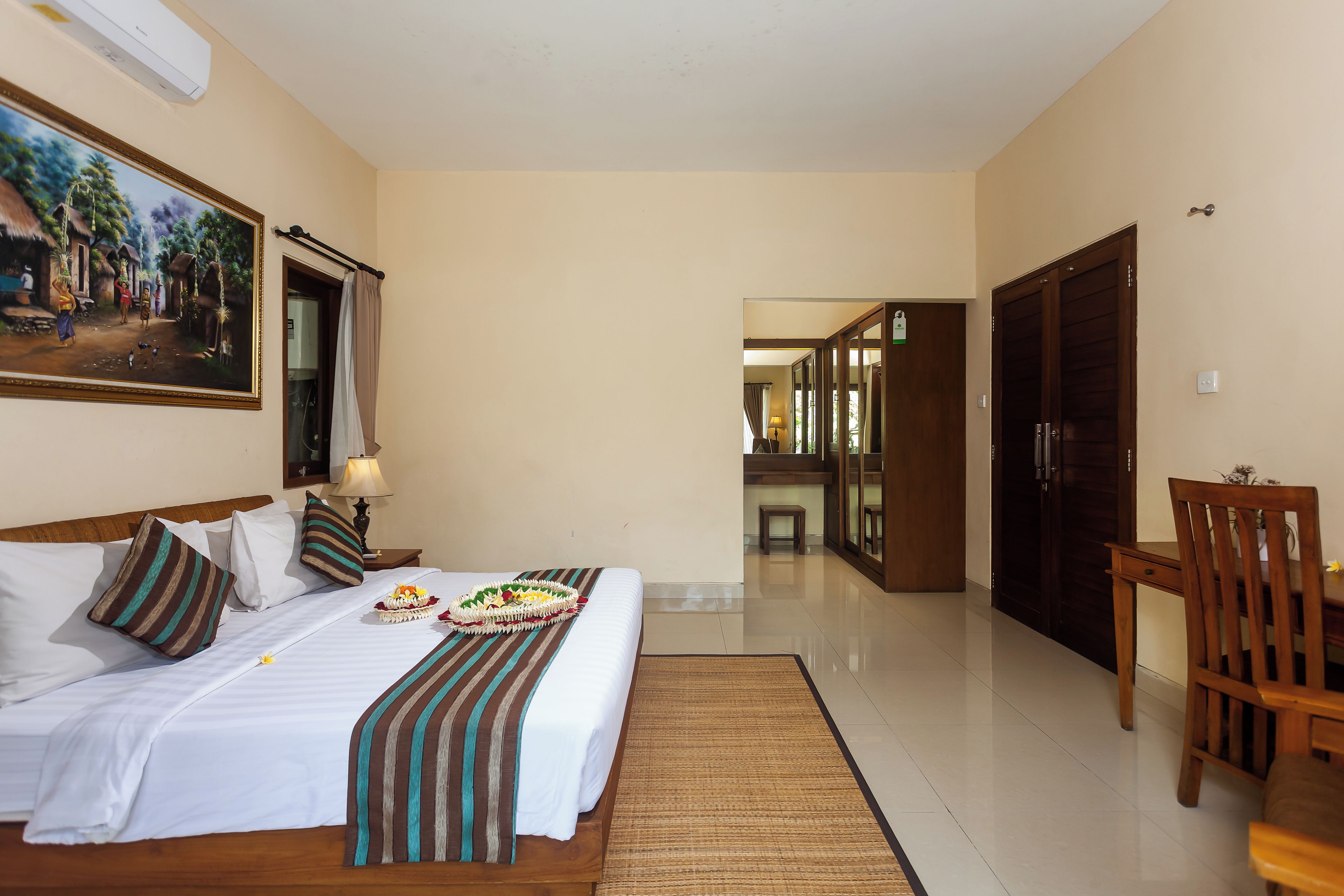 A hotel room with a large bed, a dining table, a chair, a painting on the wall, and a view into the corridor.