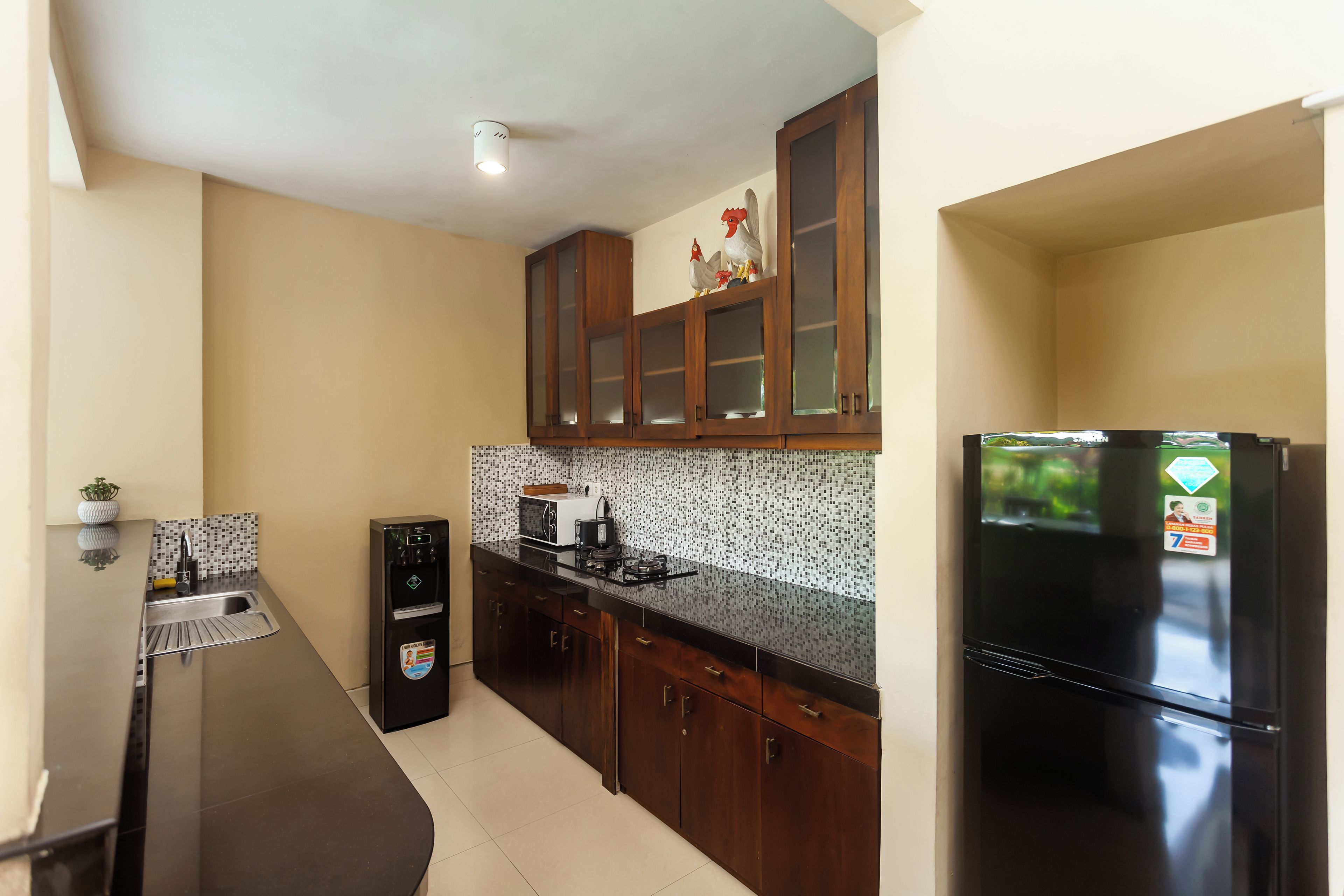 A kitchen with dark cabinets, a black refrigerator, and a microwave on the countertop.
