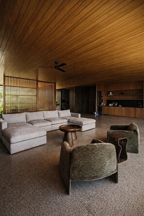 Un salon moderne avec un canapé d’angle, deux fauteuils, une table basse et un ventilateur de plafond.