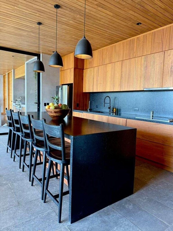 Cozinha moderna com ilha grande, iluminação pendente e armários de madeira.