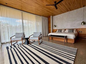 Une chambre moderne avec un grand lit, deux fauteuils, une petite table et un tapis à rayures.