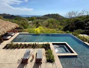 A rectangular infinity pool with lounge chairs and a small hot tub, surrounded by lush greenery and a view of the ocean. - NEW 6BR Contemporary Villa Near Santa Teresa • Ocean Views • Saltwater Pool (Santa Teresa)