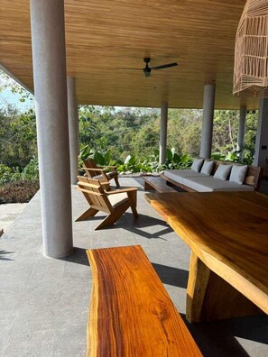 An outdoor seating area with a wooden table and chairs, a sofa, and a ceiling fan. - NEW 6BR Contemporary Villa Near Santa Teresa • Ocean Views • Saltwater Pool (Santa Teresa)