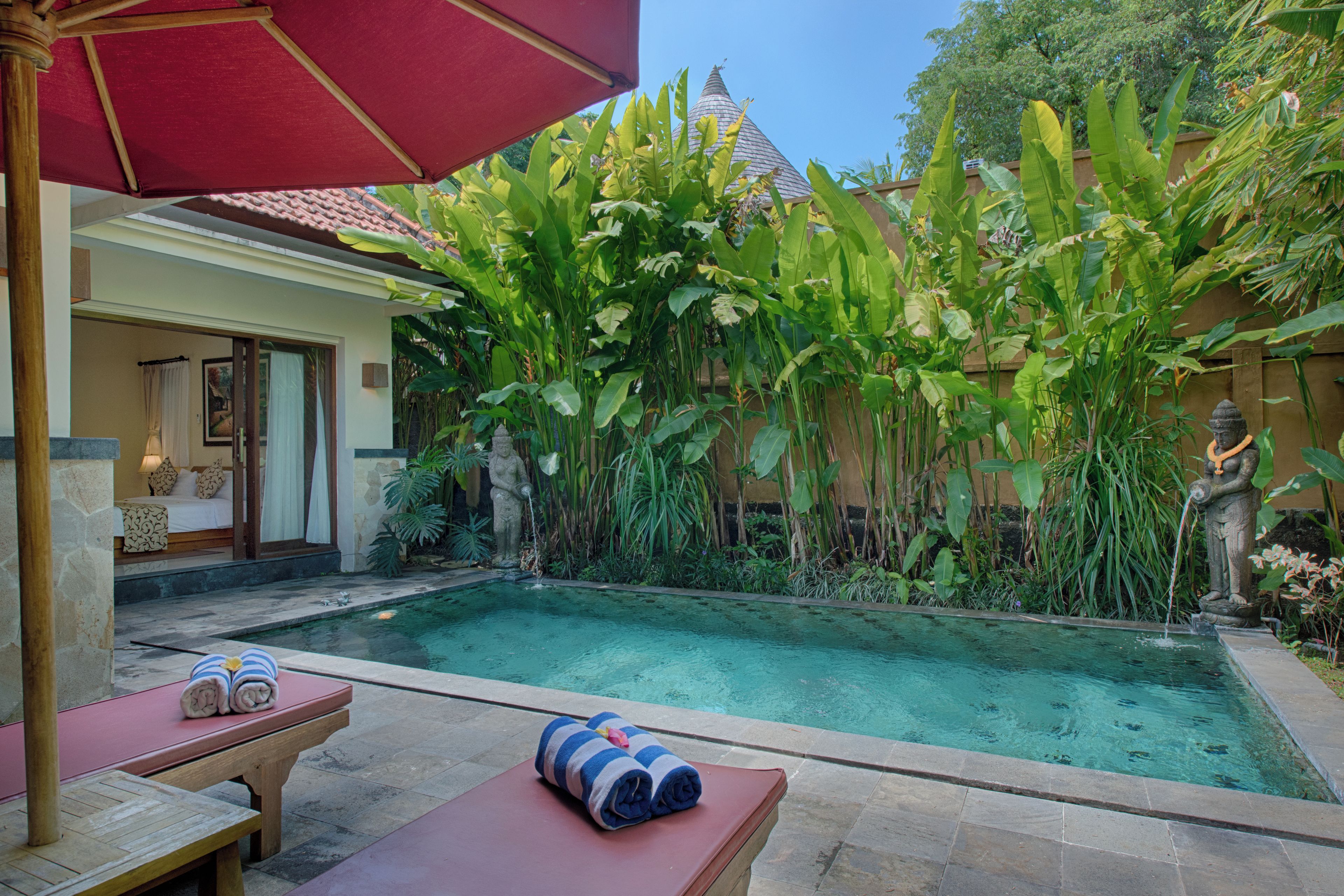 A pool area with a red umbrella, lounge chairs, and a statue.