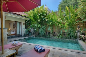 A pool area with a red umbrella, lounge chairs, and a statue. - Kadiga Villas - 2 BR pool Villa (Bali)