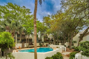 A pool surrounded by trees and buildings, with outdoor seating and a clear sky. - Elegant Sea Pines Villa Steps From The Beach (Hilton Head Island)