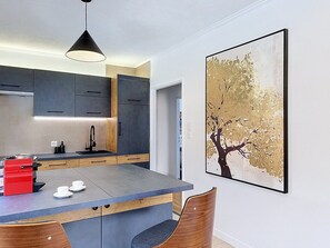 A modern kitchen with a central island, dark cabinets, and a large framed artwork on the wall. - Mercury · Mercury House 110 m² | Private parking | Train station 500 m away (Montreux)