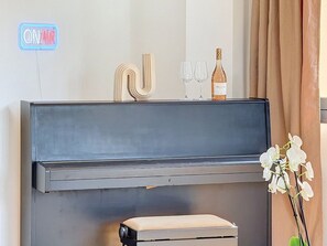 A piano with a neon sign, a bottle of wine, and a vase on top. - Mercury · Mercury House 110 m² | Private parking | Train station 500 m away (Montreux)