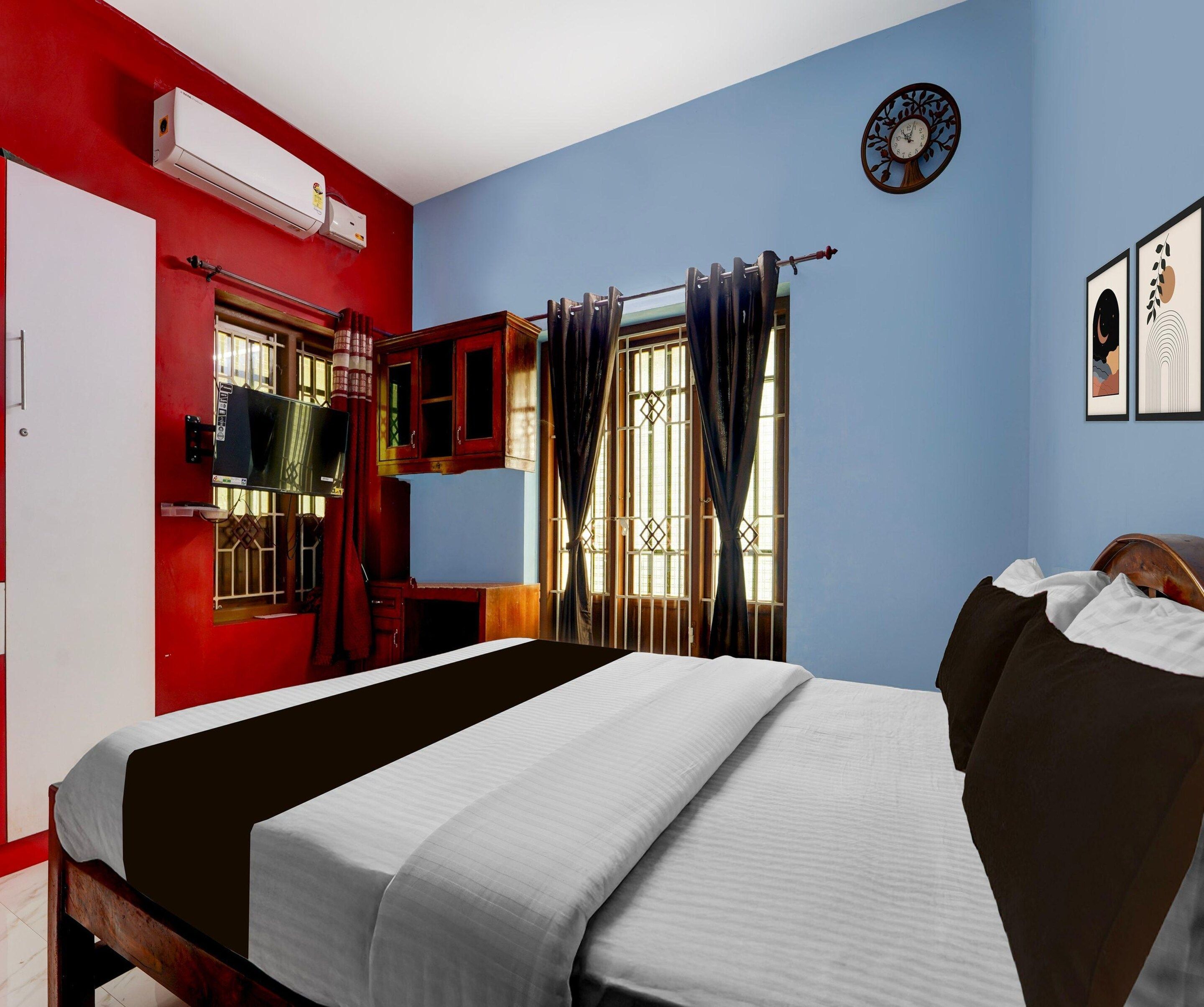A room with a bed, a television, a window with curtains, and a wall clock.