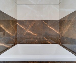 A bathroom with a white bathtub, marble tiles with brown veining, and a plain white ceiling. - Classic Balaramapuram White Castle (Neyyattinkara)