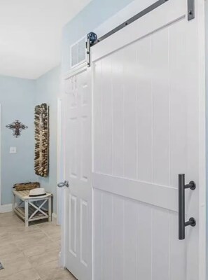 A white door with a black handle, a small table with a hat, and a wall-mounted decorative piece. - Salty Palms Penthouse, 2 BR/2 bath with Stunning Gulf Views (Panama City Beach)