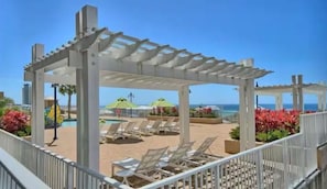 A covered outdoor area with a pool, lounge chairs, and umbrellas. - Salty Palms Penthouse, 2 BR/2 bath with Stunning Gulf Views (Panama City Beach)