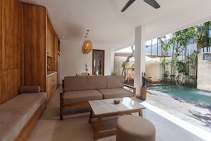 A modern living room with a wooden sofa, a coffee table, and a view of a swimming pool. - The Arca Villa - 2 BR Pool Villa (Bali)