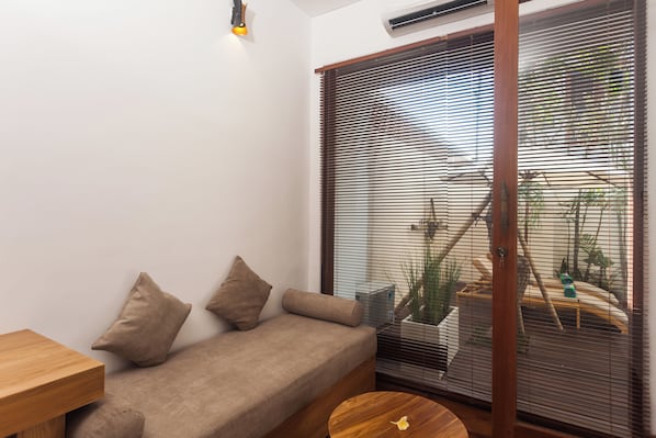 A minimalist room with a sofa, a small wooden table, and a window with blinds. - The Arca Villa - 2 BR Pool Villa (Bali)