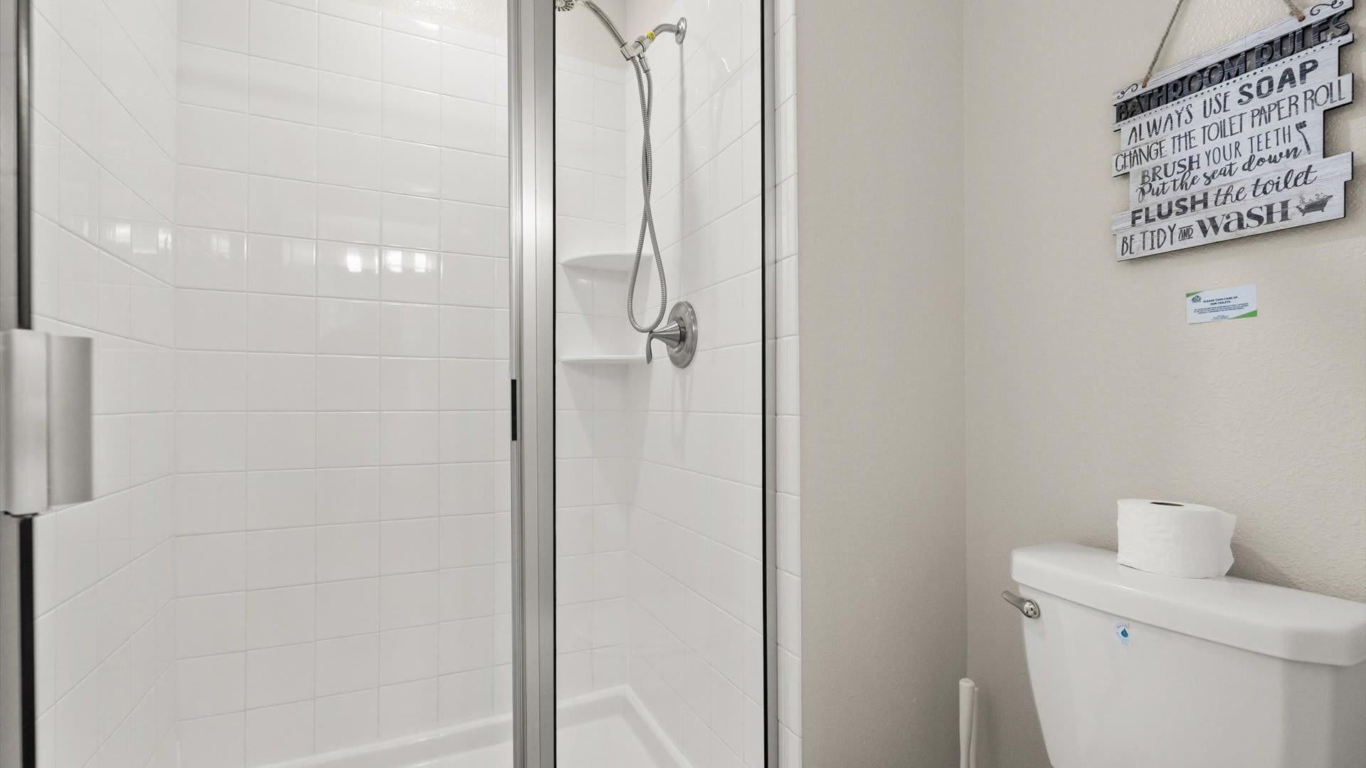 Une salle de bain avec une douche à parois de verre, des toilettes et un panneau fixé au mur contenant des conseils d'hygiène.