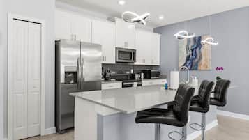 Una cocina moderna con armarios blancos, electrodomésticos de acero inoxidable, una isla central con taburetes y una lámpara de diseño contemporáneo.