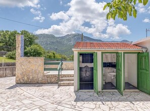A small, two-story building with a bathroom visible on the ground floor, a stone wall, and a view of mountains in the background. - Beautiful Rustic Relax Villa (Dugopolje)